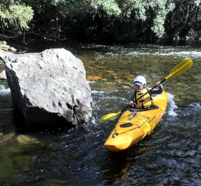 A person is paddling around the side of a large boulder during one of the Kayaking Journeys NSW operates.