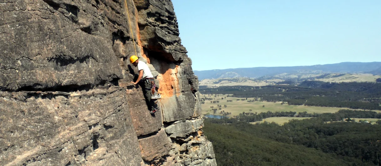A person is climbing up the face of a cliff during the Watagans Abseiling and Climbing day