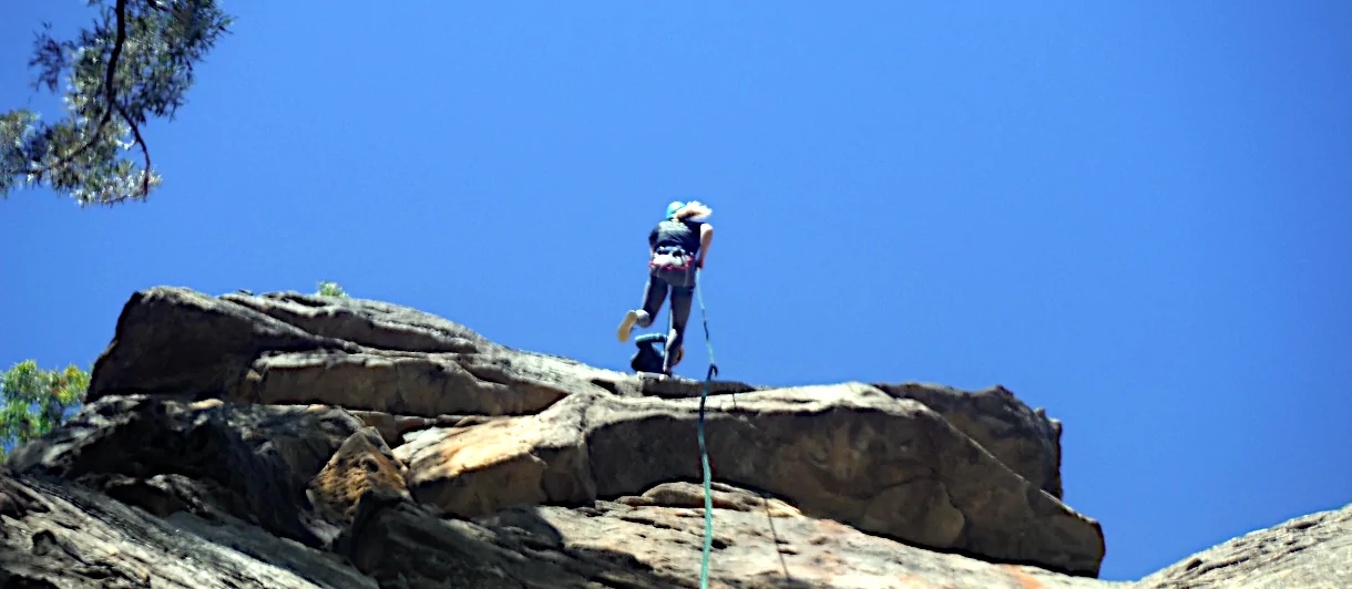 A person is Jumping down a cliff hooked to a abseil line during a NSW Abseiling Experiences day.