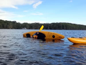 A kayak is on its side and the paddler is half in the water  learning to roll as part of Bronze Kayaking Award Journey