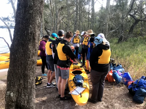 A group of students are standing around a yellow kayak during the Silver Kayaking Award Journey