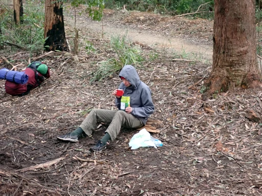 A lone hiker is eating breakfast beside the track while on the Gold Bushwalking Award Journey