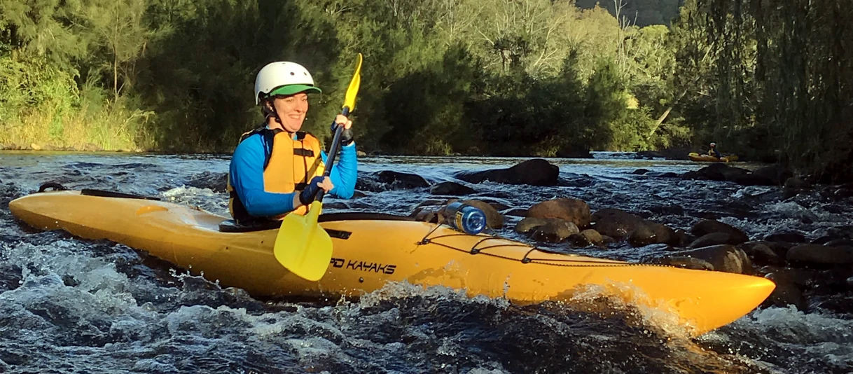 A person is paddling a Kayak down a small whitewater rapid at the start of the Barrington River Kayak Adventure