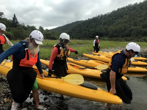 Kayaks are on the river bank during the Nymboida River Kayak Adventure and people are helping to carry them to the water