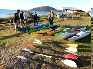 A group pf people are standing beside kayaks on the lawn getting ready to Kayak Port Stephens Broughton Island