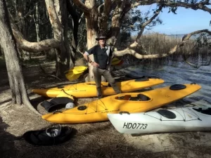 Myall Lakes Kayak Adventure guide is standing next to some kayaks on the bank of the lake