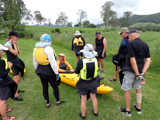 a group pf people are standing around a kayak instructor who is sitting in a kayak learning about the  Barrington River Kayak Adventure skills needed to safely paddle