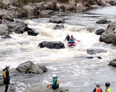 people are sitting on the shore watching rafts come down a rapid during the Snowy River whitewater rafting tour
