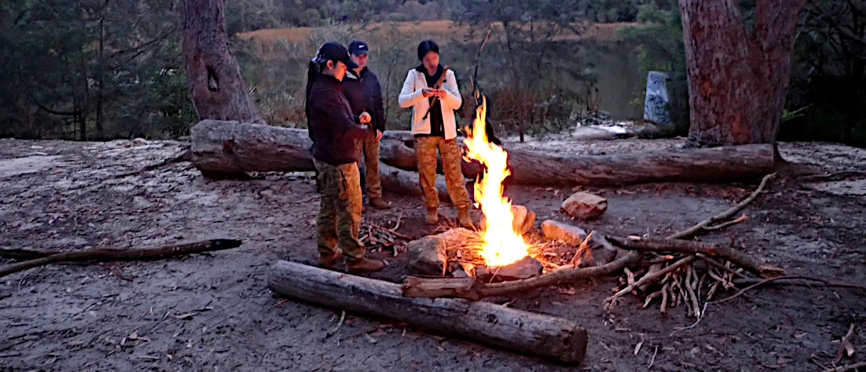 Three people standing by a roaring fire trying to get warm during a bad weather event on their Silver Qualifying Journey